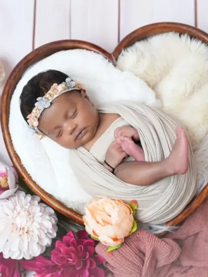Another beautiful angle of the newborn in a heart-shaped bowl, this time showing the baby's tiny feet. The floral details and soft textures make this a truly special image.