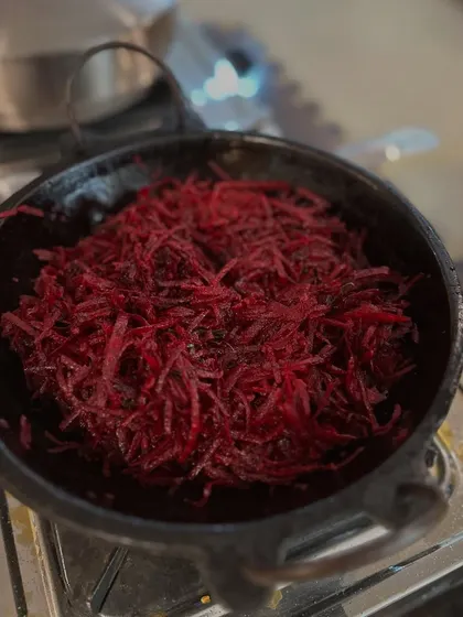 A vibrant beetroot stir-fry cooking in a traditional iron pan. Our recipes are simple, using minimal oil and spices to let the natural flavors of the vegetables shine.