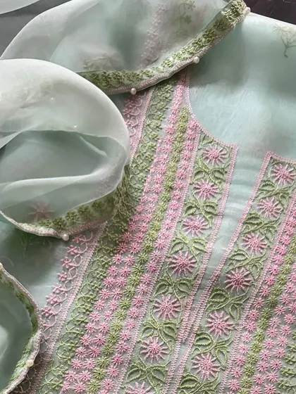 A vibrant pure organza suit in a soft sea green, adorned with intricate pink and green threadwork. The neckline features delicate work, and the dupatta is finished with a border of pearls.