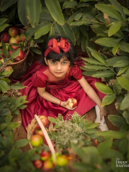 A little Snow White in an apple orchard. This high-angle shot of a girl in a red dress among the leaves is creative and enchanting.