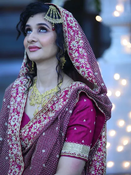 An elegant portrait of a bride in a deep magenta and gold embroidered saree, looking up thoughtfully.