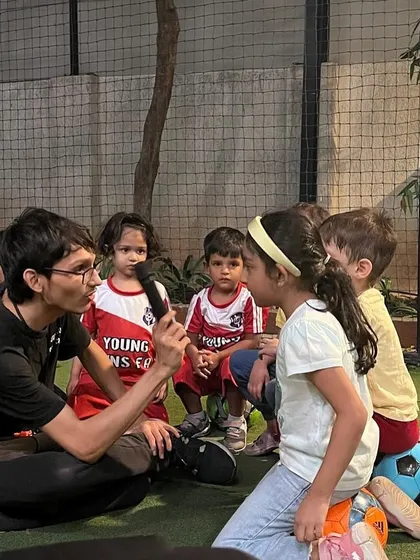 A coach kneels down to speak with a child at her level, holding a microphone to make her feel special. We believe in listening to our students and valuing their voices.