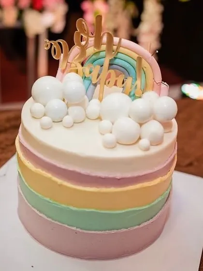 A cheerful pastel rainbow cake perfect for a baby shower or first birthday. The cake features soft, blended rainbow stripes and is topped with fondant clouds and a "Baby" topper.