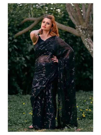 An elegant outdoor portrait in a black sequined saree. The natural setting provides a beautiful contrast to the glamorous attire.