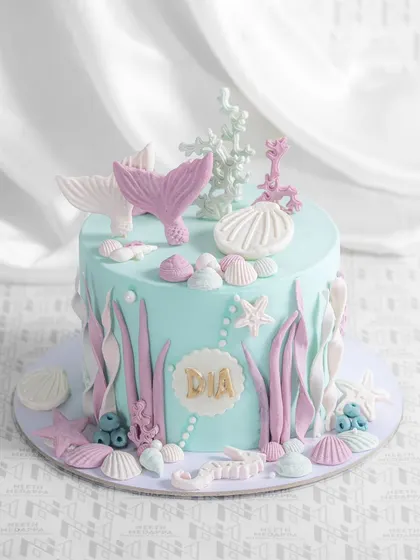 A beautiful mermaid-themed cake, with delicate mermaid tails, seashells, and coral crafted from fondant in pastel shades of blue and pink.