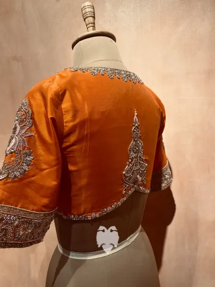 The back of an orange and hot pink blouse, showing the symmetrical embroidered motif that adds an elegant finish.