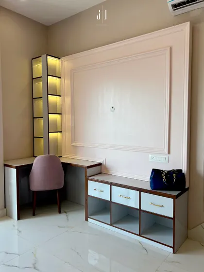 A bedroom study and storage unit designed in soft pink and white tones. The illuminated shelving adds a touch of elegance while providing functional space for work and display.
