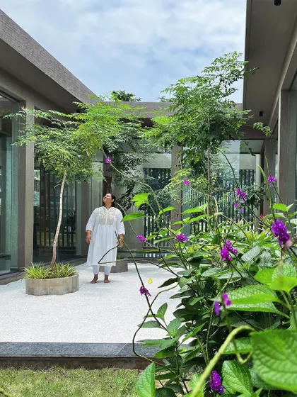 A view from within the courtyard garden, where purple flowers add a touch of wild color against the structured green and white palette. It's a space designed for quiet reflection, surrounded by the grace of trees.