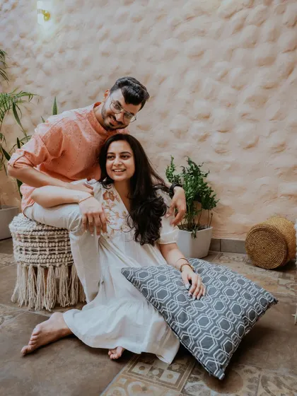A playful and happy portrait of the couple in a bohemian-style indoor setting, their relaxed poses reflecting their comfortable love.