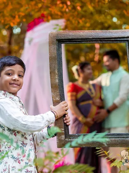 A creative maternity photo where the older brother holds up a frame, perfectly capturing his parents in a loving pose in the background. This is a fun and unique way to announce a new arrival.