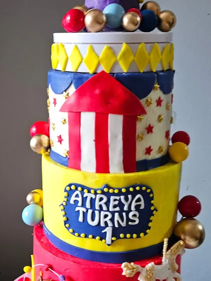 A close-up view of the vibrant, multi-tiered carnival cake, showing the detailed fondant work of the tent, stars, and personalized name plaque.
