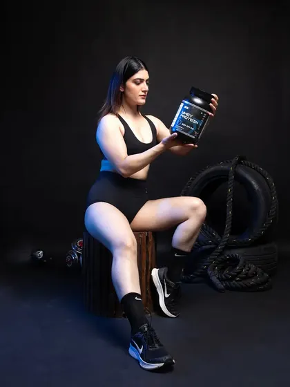 A female model seated and holding a whey protein container, looking directly at the product. This pose suggests product trust and endorsement.