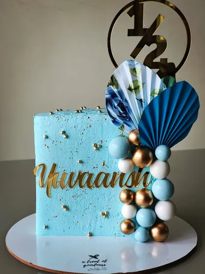 Milestone celebrations aren't just for adults. This stylish square cake was for a half-year birthday, featuring a sky-blue buttercream, a cascade of decorative spheres, and elegant paper fans.