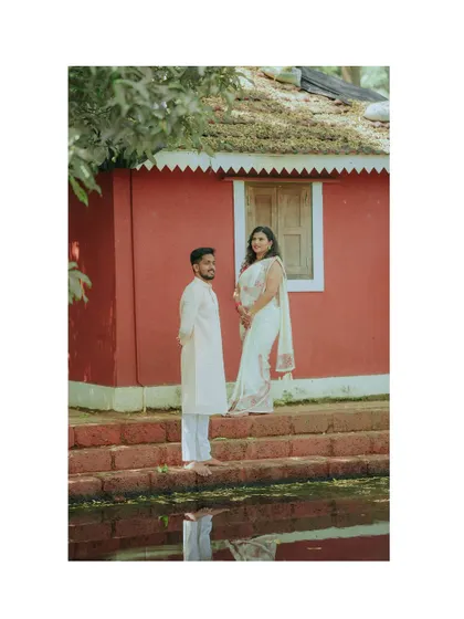 A simple, elegant portrait against a rustic red wall. The couple's traditional white outfits create a beautiful contrast in this serene pre-wedding photo.
