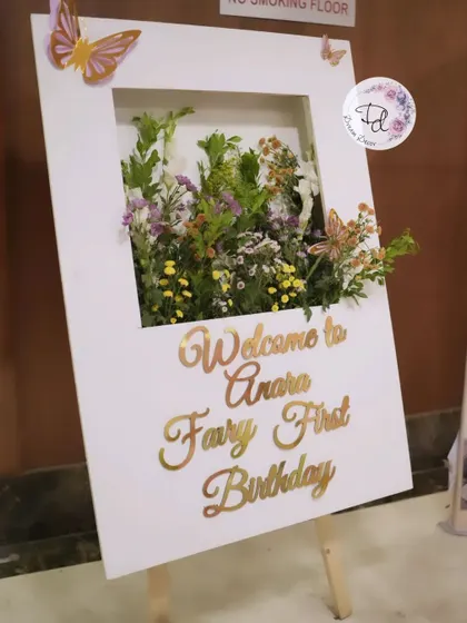 A welcome sign for a 'Fairy First Birthday'. The sign itself is a beautiful prop, with a built-in shadow box filled with flowers.