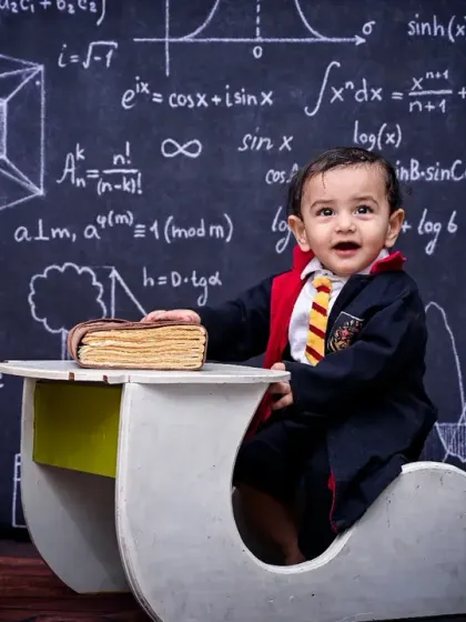 A wide shot of the Harry Potter themed photoshoot, showing the little wizard at his desk with a globe, books, and vintage cameras. The detailed set creates a magical atmosphere for the portrait.