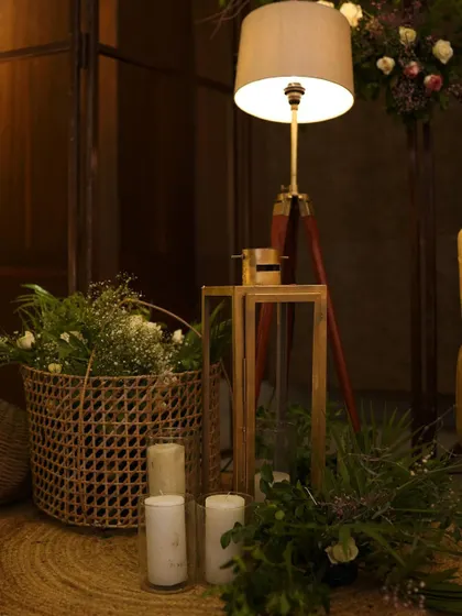 A cozy corner featuring a modern floor lamp, a woven basket filled with baby's breath, and pillar candles. This setup creates a warm and inviting nook for guests.