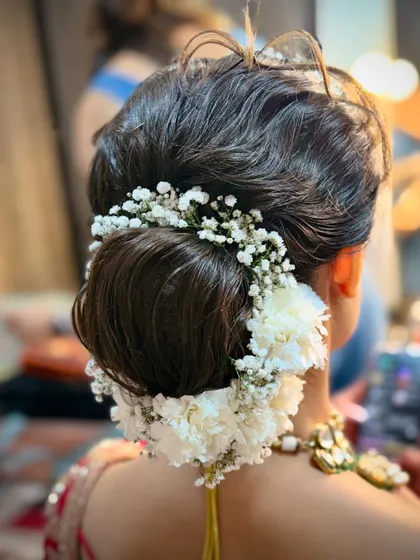 A beautiful hairstyle completes the look. This is a classic bridal bun, intricately woven and adorned with fresh baby's breath and carnations for a touch of soft, romantic elegance.