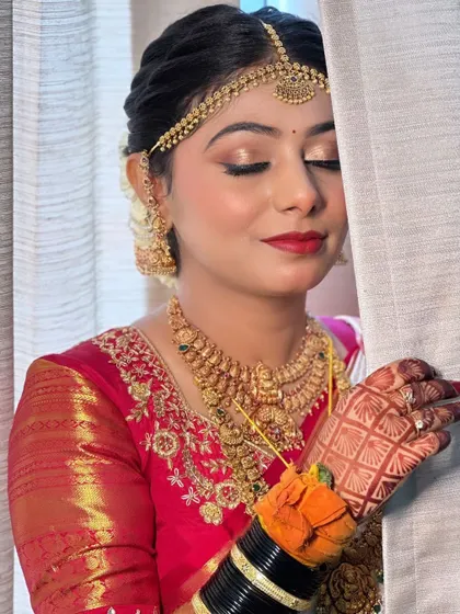 A serene moment captured before the ceremony. Her makeup features a soft gold eyeshadow and a classic red lip, a timeless combination for any South Indian bride.