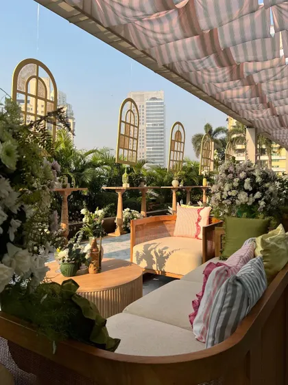 A cozy lounge corner for a Haldi, with wooden sofas, pastel cushions, and hanging window-frame props creating a whimsical garden feel.