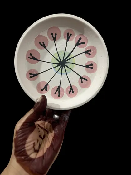 A hand-painted plate held by a henna-adorned hand. The process of painting pottery is just as beautiful as the finished piece, a dance of color and creativity.