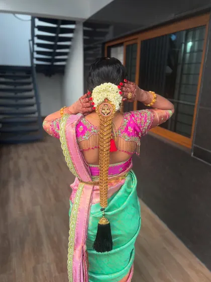 A bride adjusting her hair, showing a full gold 'Jadai Alangaram' on a thick braid. This style is built to be secure and withstand all the movements of a wedding day.