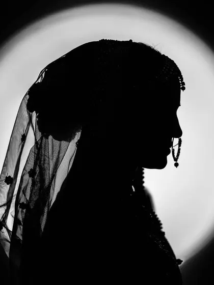 A dramatic silhouette of the bride against a circular light source. This black and white image is artistic and mysterious, highlighting the iconic shape of a bride with her veil and nose ring.