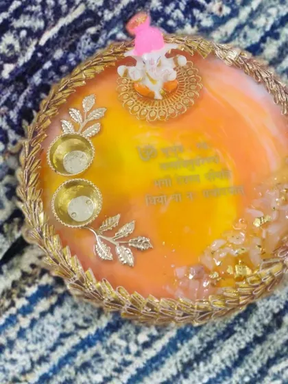 A bright and sunny pooja thali in shades of orange and yellow. It's decorated with a delicate golden lace border, silver leaf accents, and a small Ganesh idol for blessings.