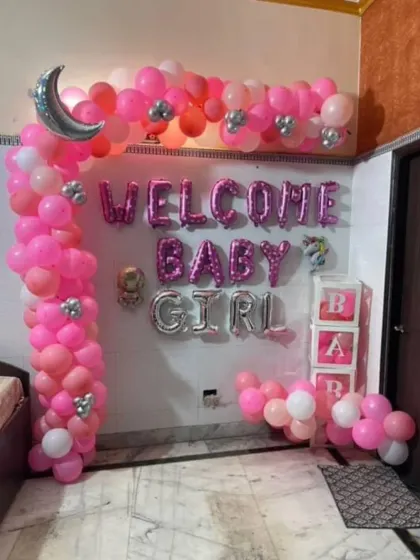 A clear, straight-on shot of the pink and silver balloon arch with 'Welcome Baby Girl' foil letters and transparent 'BABY' blocks filled with balloons.