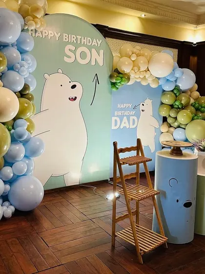 A full view of the "We Bare Bears" birthday decor, showing the two backdrops and the complete balloon arch. The wooden ladder shelf adds a rustic touch and a place for additional displays.