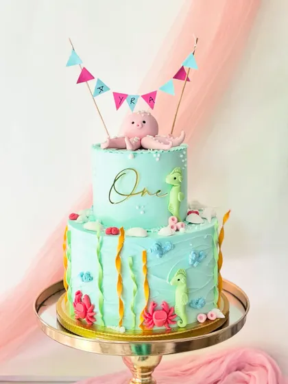A two-tiered "under the sea" cake for a first birthday. This design features a cute octopus topper, seahorses, crabs, and seaweed, all made from fondant.