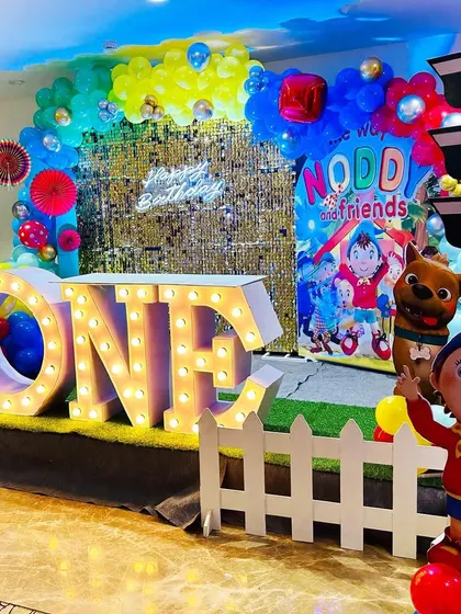A full view of the Noddy-themed first birthday stage, with a gold shimmer wall and "ONE" marquee letters.