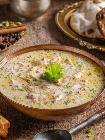 A creamy Chicken Malai soup, garnished with fresh parsley and served with breadsticks, shot in a warm, inviting style.