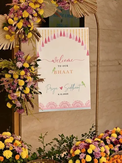 A welcome sign for a 'Bhaat' ceremony, decorated with pampas grass and colorful flowers.