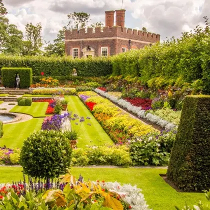 An example of a classic English garden, characterized by colorful, overflowing flowerbeds, neatly trimmed lawns, and shaped topiaries. This style creates a romantic and picturesque landscape.