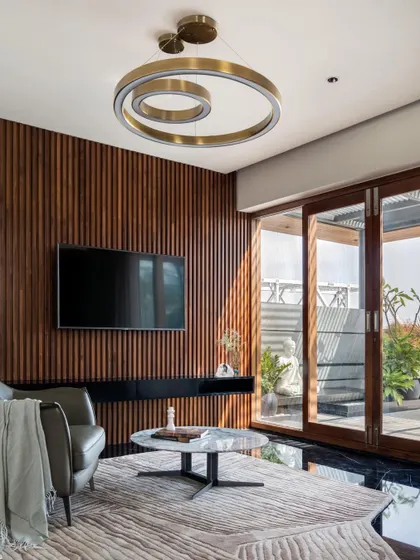A family lounge at Timber Edge, where a vertically slatted timber wall serves as a feature backdrop for the television, opening onto a terrace.