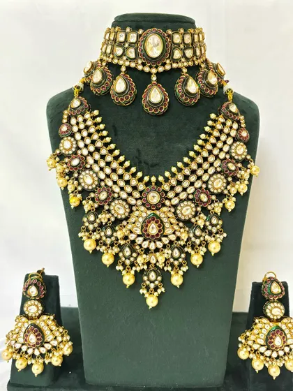 A heavy bridal necklace set with a wide, web-like design. This rental piece is adorned with Kundan, pearls, and Meenakari work.