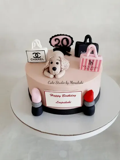 A fun 20th birthday cake for someone who loves their dog, makeup, and shopping. It features handcrafted toppers of a puppy, lipstick, and bags from Chanel and Victoria's Secret.