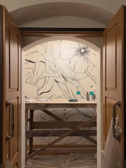 The beginning of a monochrome floral mural, seen through an arched doorway. This work-in-progress shot captures the anticipation of a blank wall about to bloom with art.