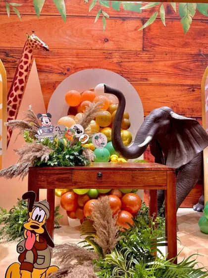 This close-up shows the intricate details of the jungle party decor. An elephant and giraffe prop are set against a wood-paneled backdrop, with Mickey and Pluto cutouts adding a touch of Disney magic.