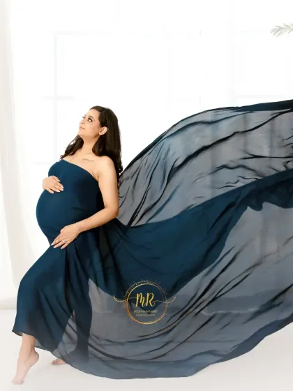A dynamic solo portrait using a flowing teal fabric. The fabric is tossed to create a wave-like effect, highlighting the mother's silhouette against a clean, white background.
