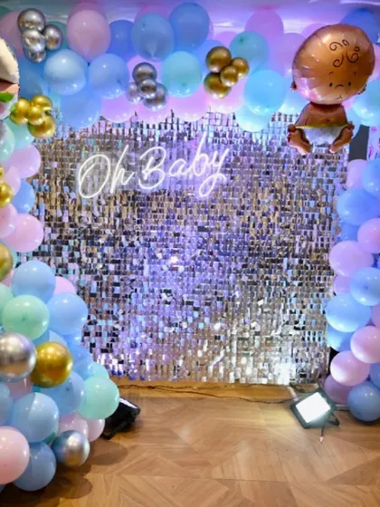 An "Oh Baby" themed baby shower with a silver shimmer wall. The backdrop is framed by pastel pink, blue, and green balloons.
