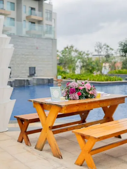 A rustic picnic table and benches are set up by the pool for a casual pre-wedding event.
