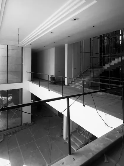 The interior of a double-height living room during construction. Even with bare walls and scaffolding, the grand scale, tall windows, and ceiling details hint at the bright, open, and dramatic space it is planned to become.
