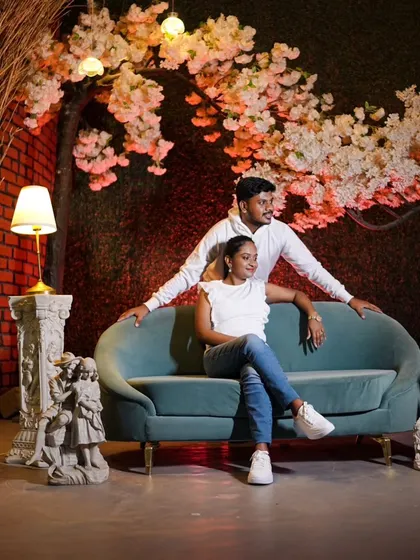A beautifully composed indoor shot with the couple relaxing on a couch against a floral backdrop. The lighting and setup create a cozy, elegant feel.