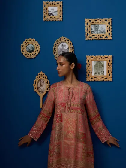 This shot uses the gallery wall as a framing device, creating a visually interesting composition. The model's pose is open and inviting, showcasing the ethnic wear in a lifestyle context.