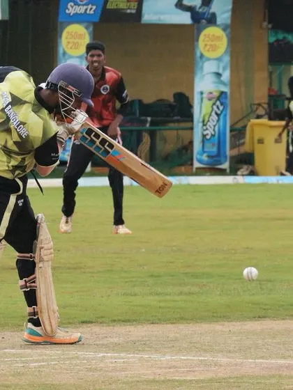 A powerful shot from a batter during a Dasara Cup match, with spectators in the pavilion.