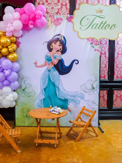 A dedicated tattoo station with a beautiful Princess Jasmine backdrop, perfect for a Disney-themed party.