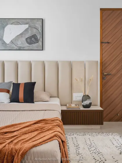 This bedroom is defined by a warm neutral color palette, creating a cozy and minimal space. The upholstered headboard, wooden accents, and abstract art come together to form a calm and inviting retreat.