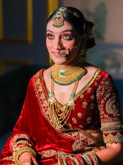 A beautiful portrait of the bride in her red velvet lehenga. The soft lighting and her elegant pose highlight the richness of the fabric and her traditional jewelry.